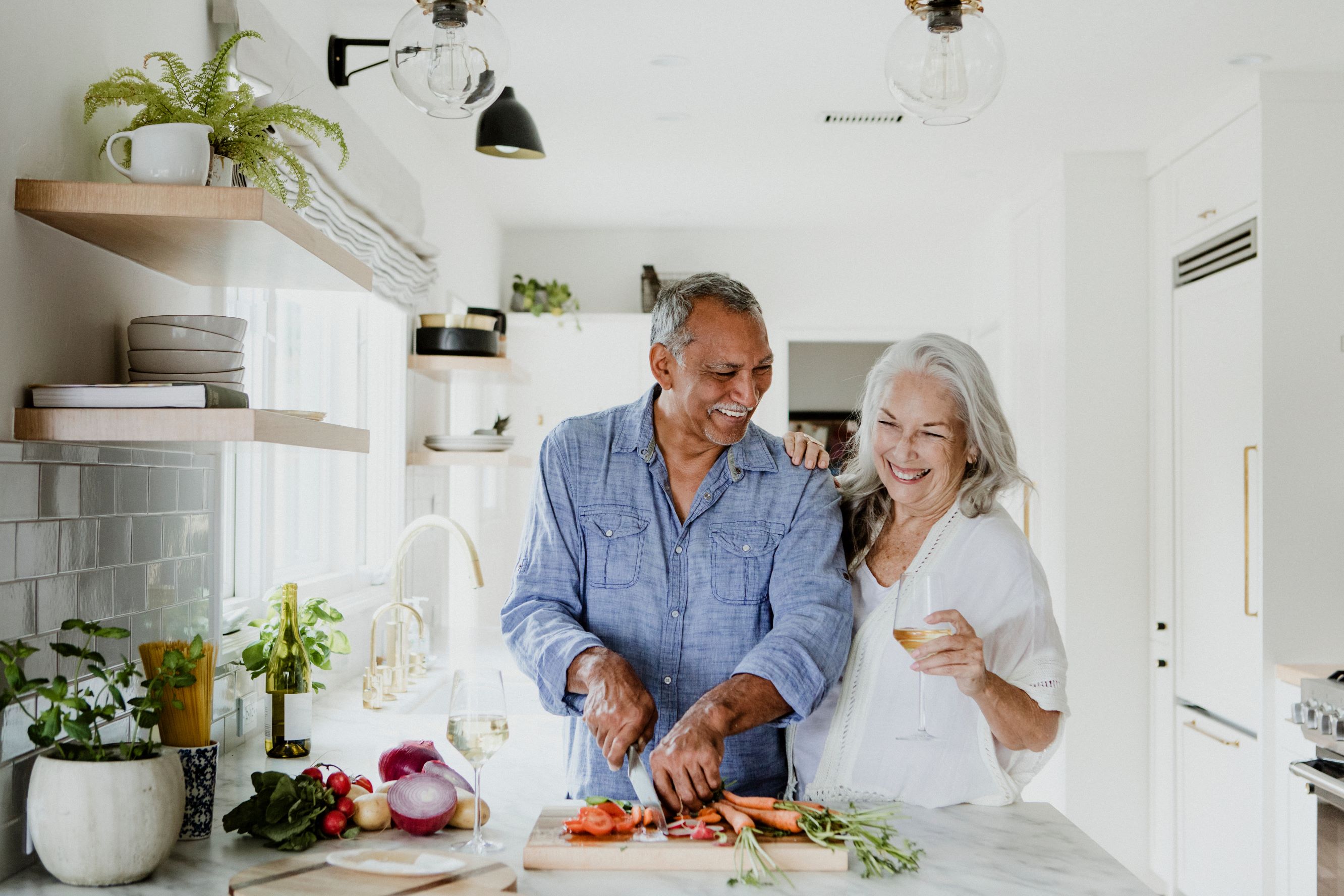 Retired senior couple smiling as they prepare a meal in their kitchen.